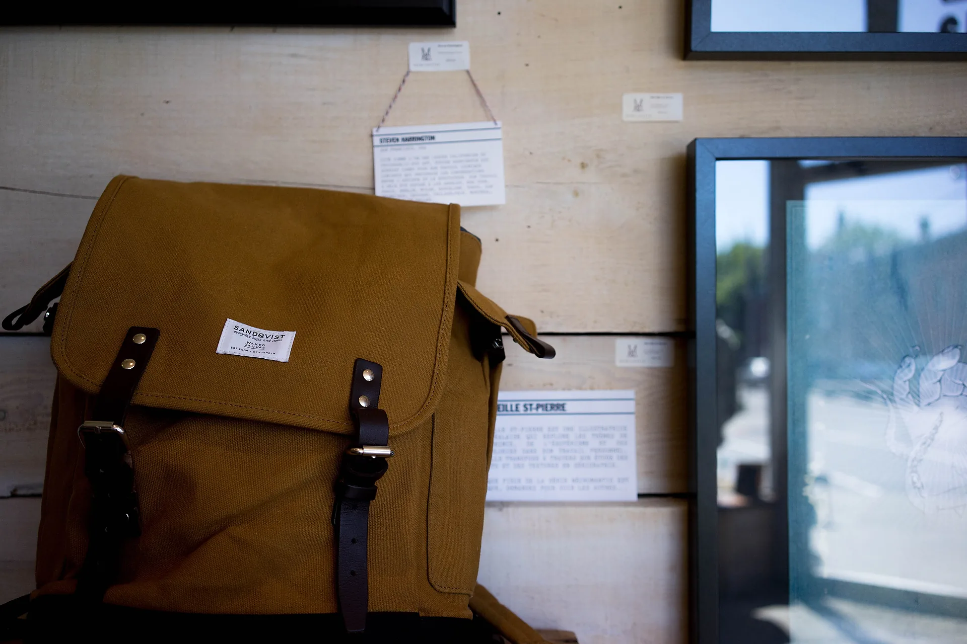 A canvas and leather backpack standing against a studio wall