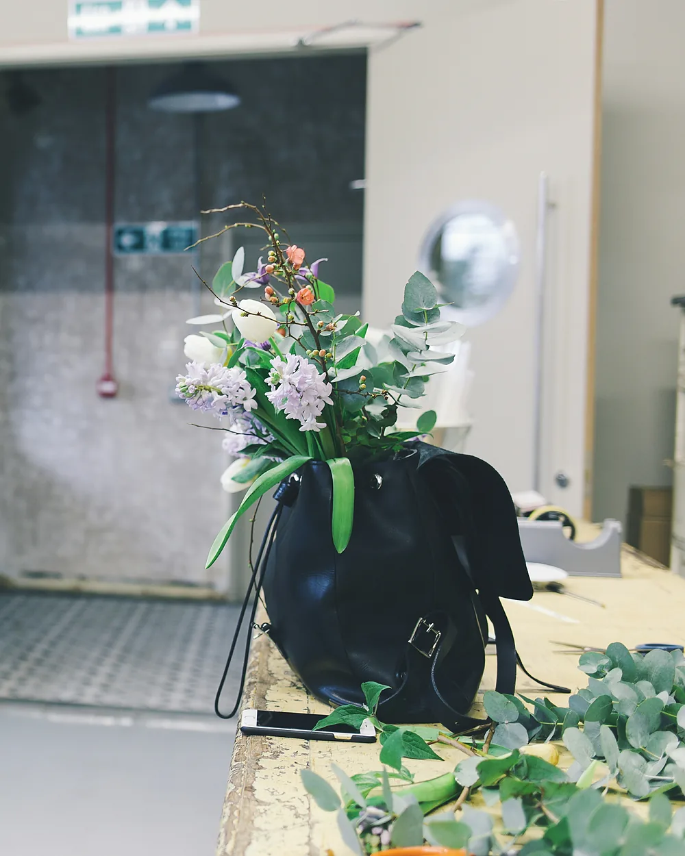 A structured black leather handbag photographed against a pale wall