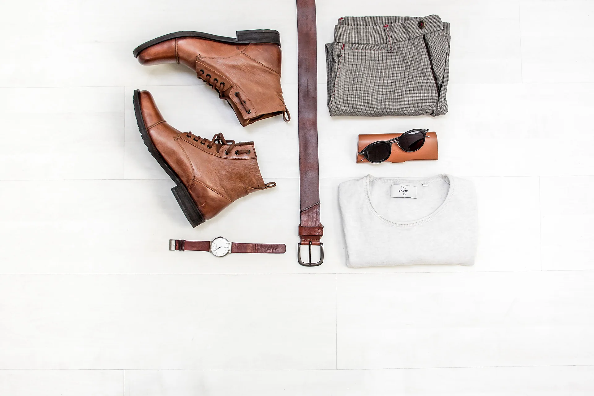 A leather tote laid out with boots, a belt and a watch in a flatlay