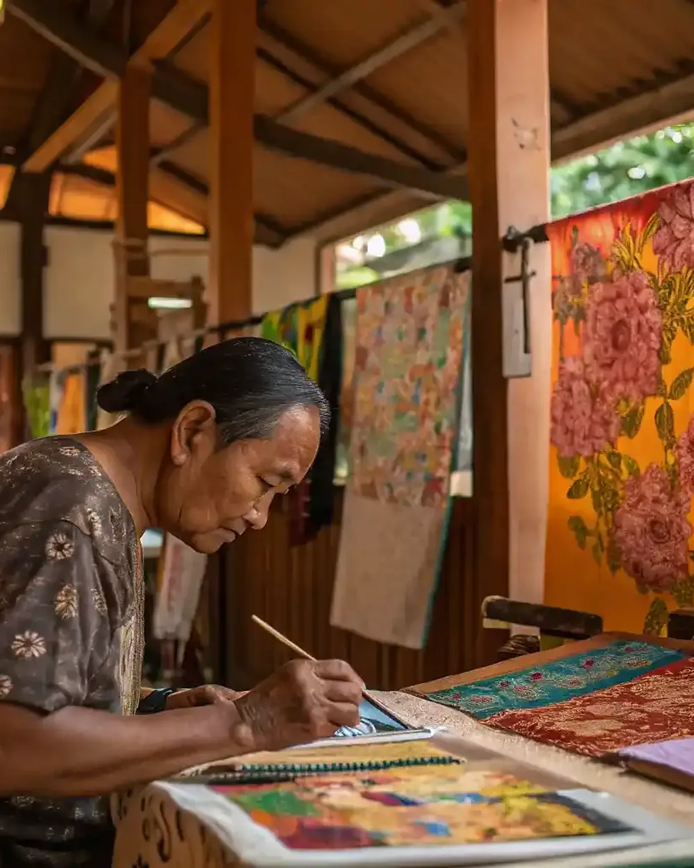 A Balinese artisan hand-painting batik at a workshop table