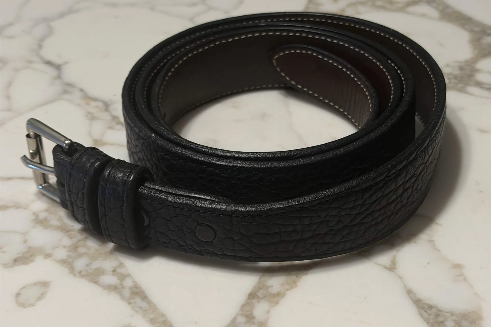 A black leather belt coiled on a marble surface