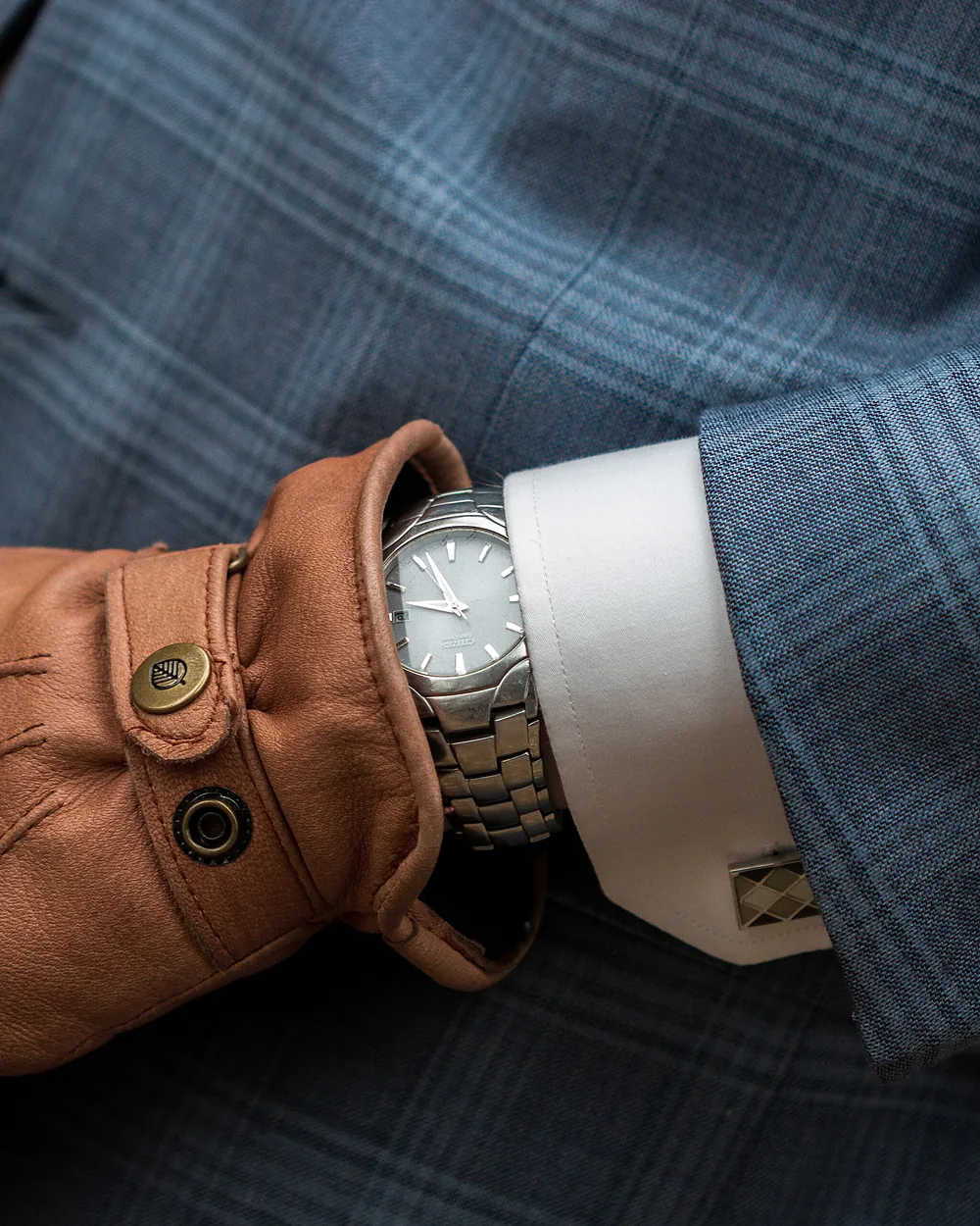 A tan leather glove and a wristwatch against a tailored sleeve