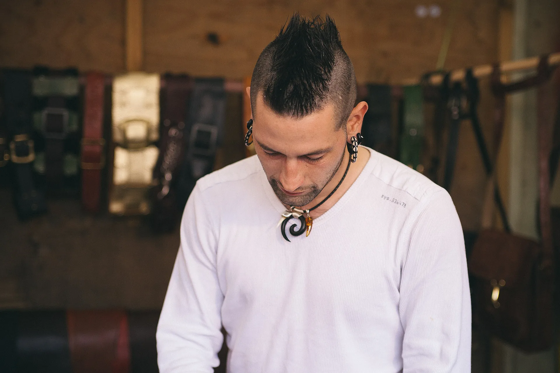 A leatherworker at the bench with finished belts and straps hanging behind him