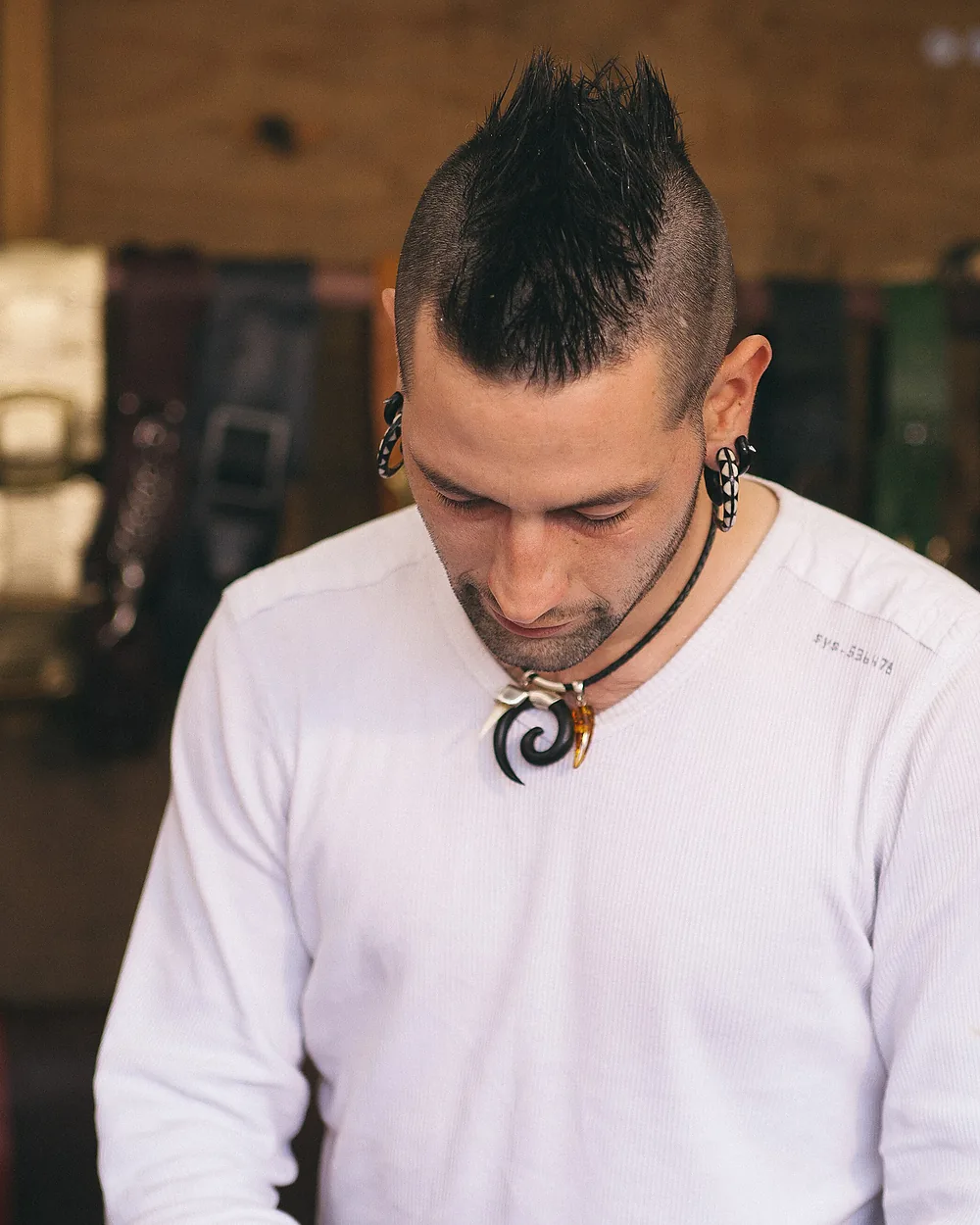 A leatherworker at his bench with finished belts hanging behind him