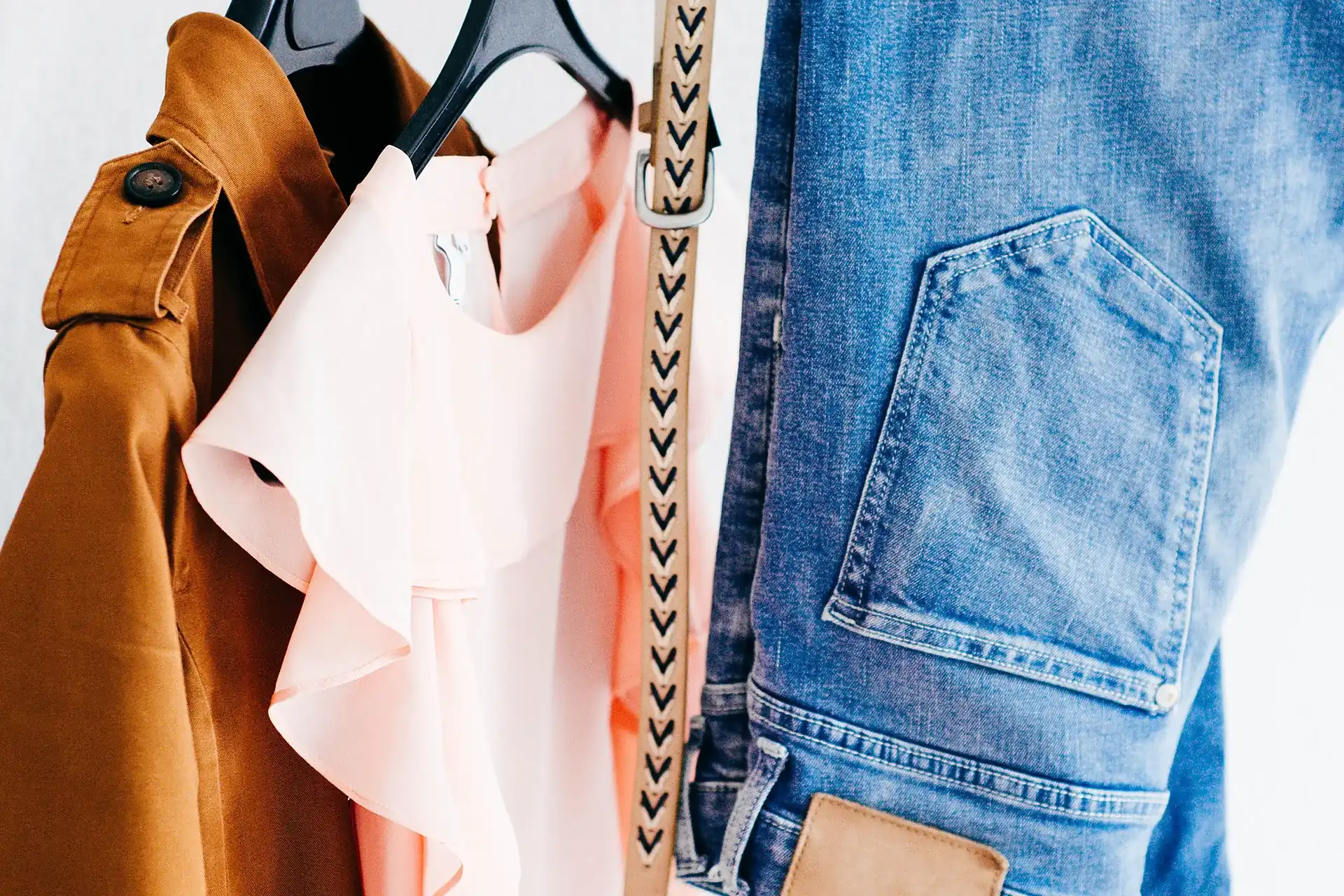 A tan leather jacket hanging on a rail beside other garments