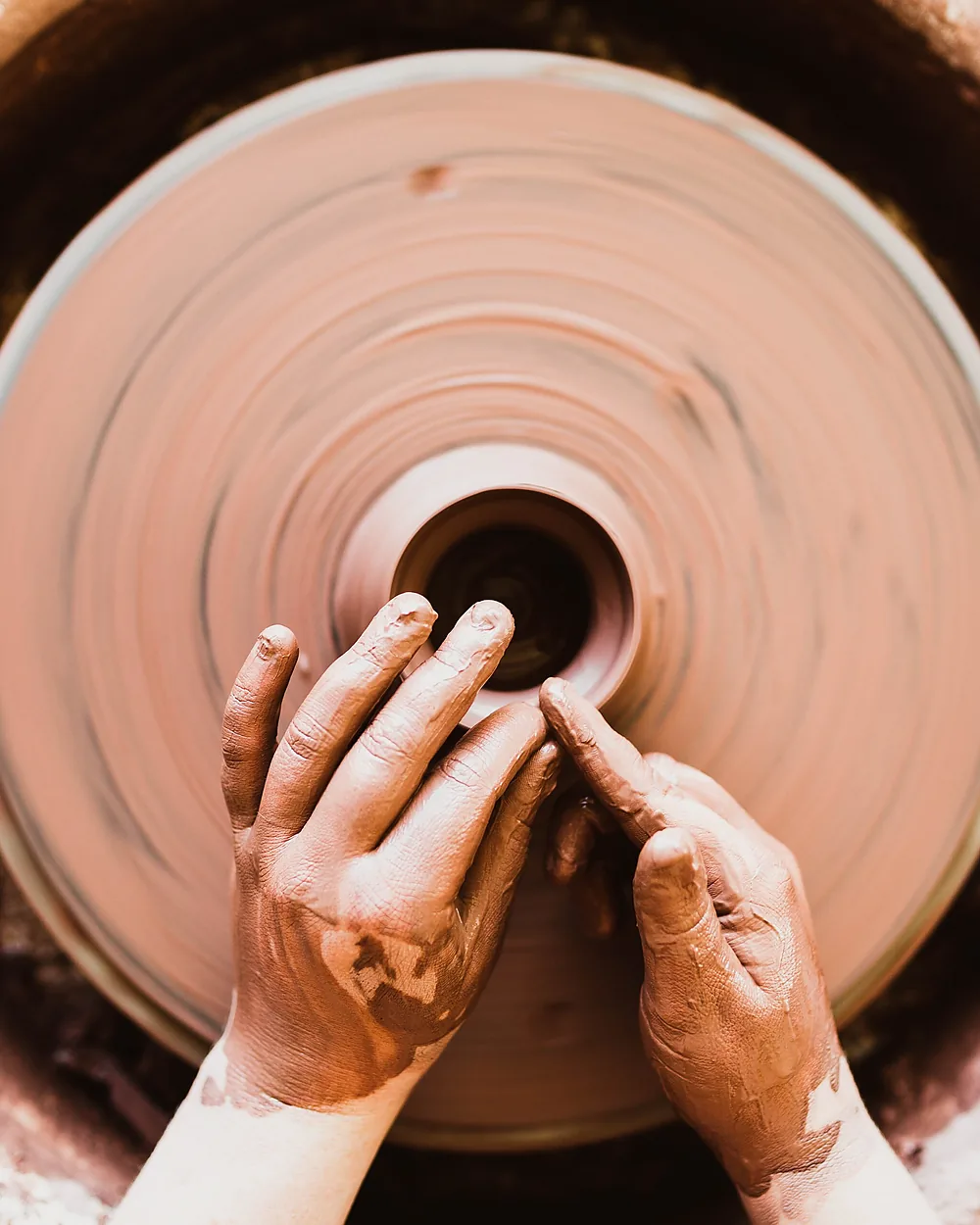 A pair of hands shaping clay on a potter's wheel