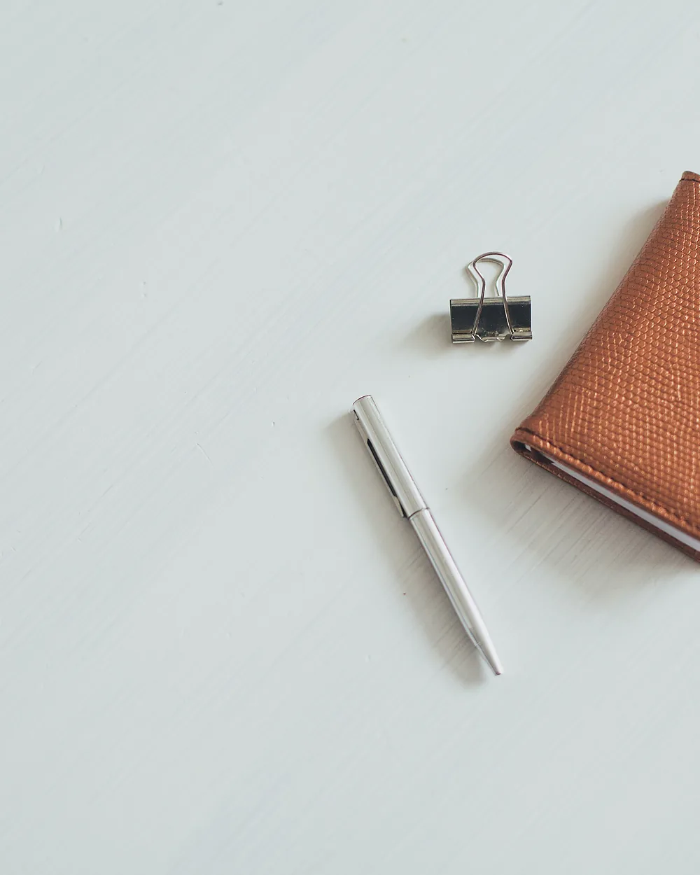 A tan leather card wallet beside a pen on a white desk