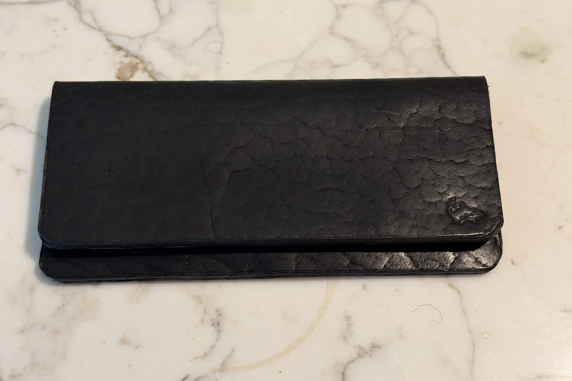 A slim black leather long wallet on a marble surface